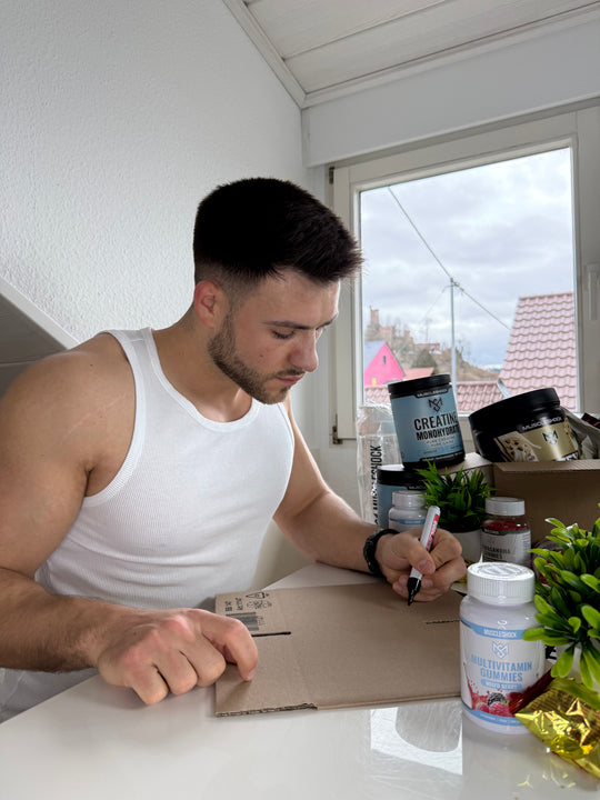 Ein Mann schreibt eine Nachricht auf einen Versandkarton neben Muscleshock Supplements.