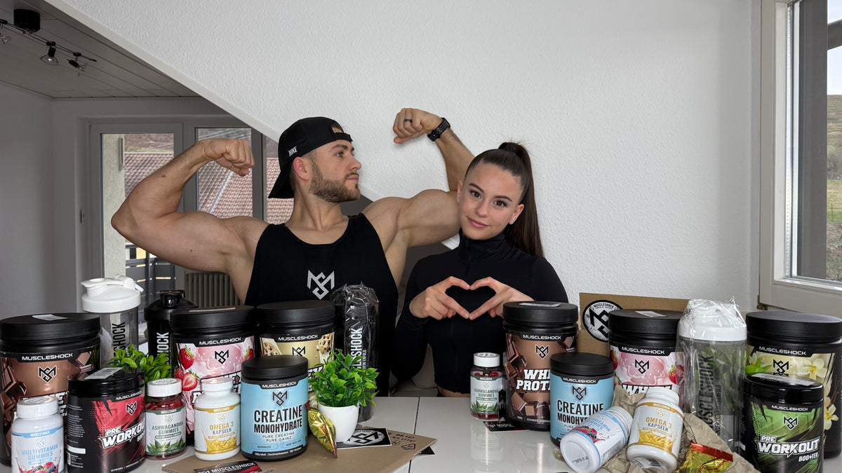 Zwei Personen mit Muscleshock-Produkten auf dem Tisch – er zeigt den Bizeps, sie formt ein Herz mit den Händen