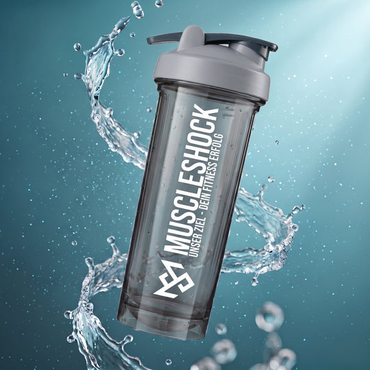 Muscleshock NXTGN Protein Shaker Nebula Grey: rauchgrau durchscheinender Becher mit hellgrauem Deckel, dunklem Klappverschluss und Aufdruck „Unser Ziel – Dein Fitness Erfolg“, umgeben von einem Wasserwirbel.